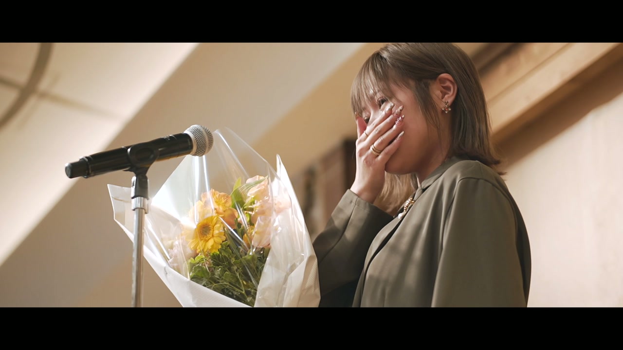 花束を手に、壇上で涙をこらえるスタッフ