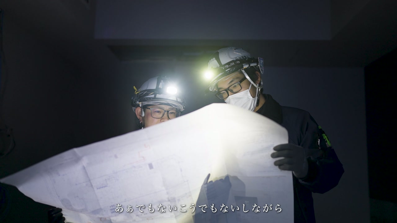ヘッドライトの明かりで図面を確認する二人