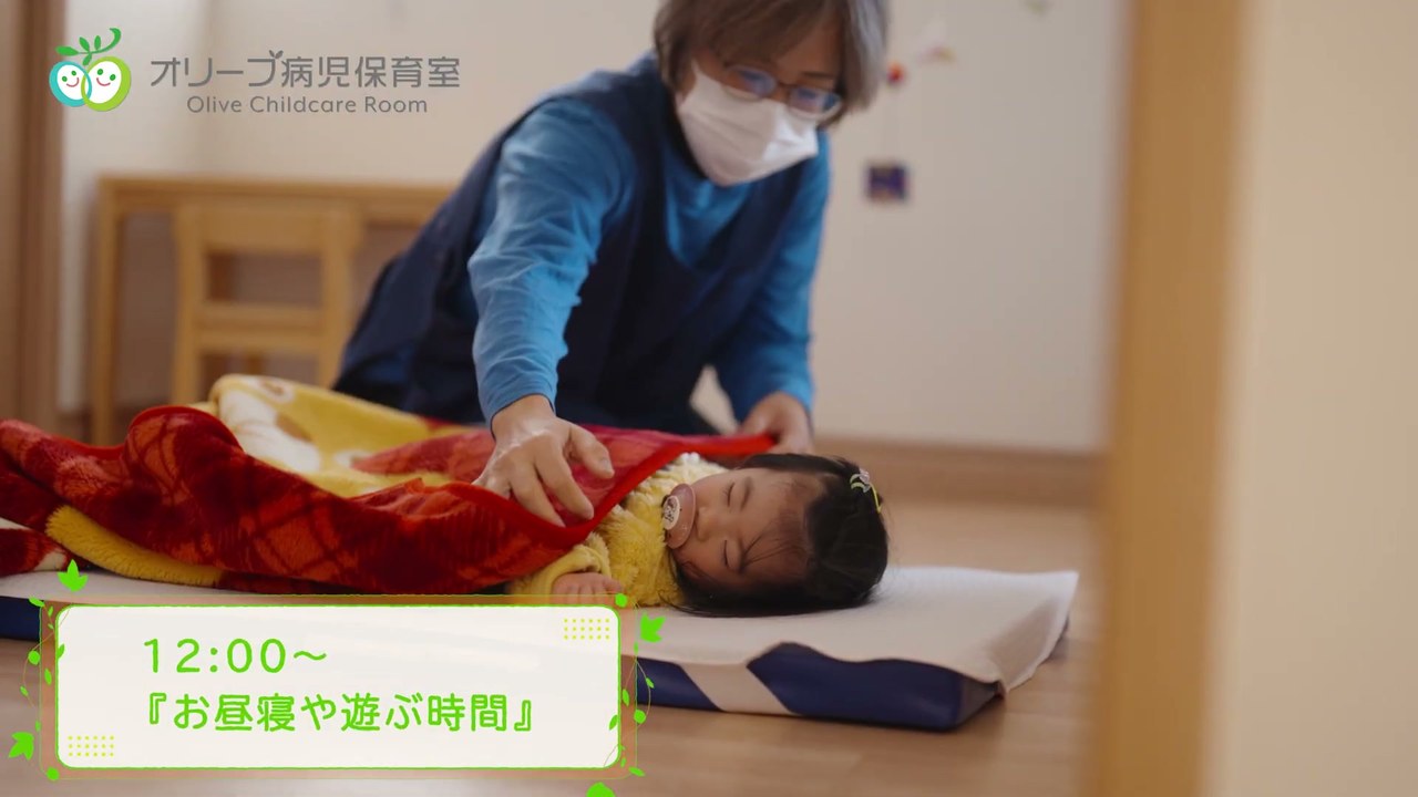 お昼寝するお子さんに寄り添う保育士 /「12:00〜 お昼寝や遊ぶ時間」